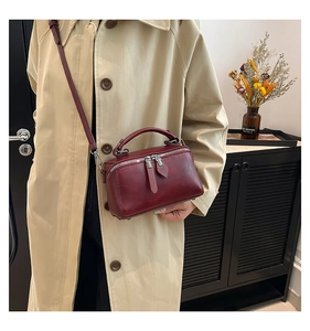 Detail of burgundy leather crossbody bag featuring dual zippers and top handle with model