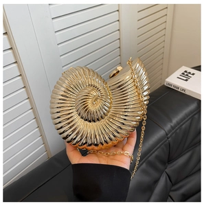 Macro shot of snail-shaped gold evening clutch bag with spiral metal texture and chain