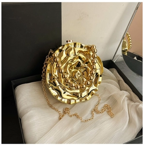 Detail of a golden rose-shaped clutch with pearlescent handle and fine chain strap