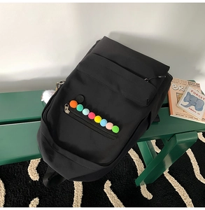 Close-up of black nylon backpack featuring colorful pom-pom details on green bench