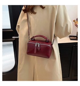 Detail of burgundy leather crossbody bag with dual zippers and matching top handle