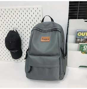 Detail of grey nylon backpack featuring leather logo tag and multiple zipper pockets