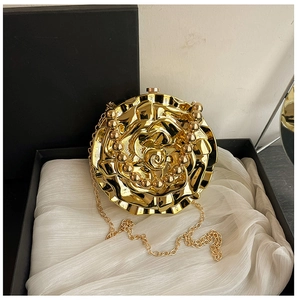 Macro detail of golden rose-shaped metal clutch with pearl handle in a black gift box