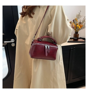 Detailed view of dark red rectangular handbag with double zippers on beige coat