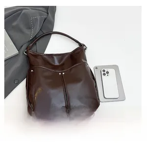 Vue détaillée du grand cabas en cuir verni marron foncé avec rivets pour comparer la taille