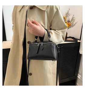 Detail of a black minimalist box-shaped crossbody bag shown on a trench coat model