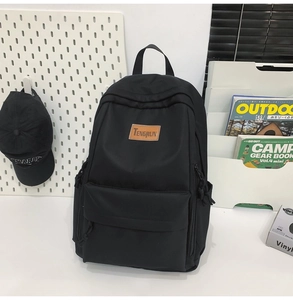Detail of minimalist black student backpack featuring a brown leather brand logo patch