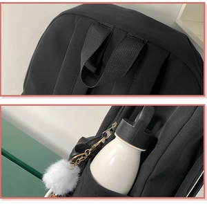 Detail of black backpack showing reinforced handle, side pocket with bottle and plush charm