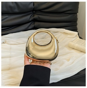 Detalle de bolso de mano media luna en acrílico dorado con asa redonda y correa de cadena