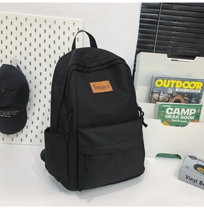Detail of waterproof black nylon backpack featuring a leather logo patch and multi-pocket design