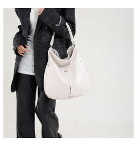 Détail du sac hobo blanc brillant avec rivets argentés porté à l'épaule d'un mannequin