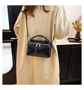 Detail view of black glossy leather crossbody bag with silver zippers and handles