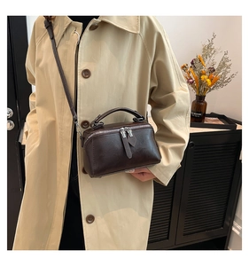 Detail of a dark brown vintage crossbody bag with silver zippers shown on a khaki trench coat