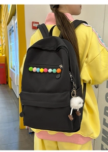 Detailed view of black canvas backpack with colorful pom-poms and cute plush charm pendant