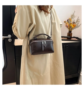 Detail of dark brown box-style handbag worn by a model in a beige trench coat