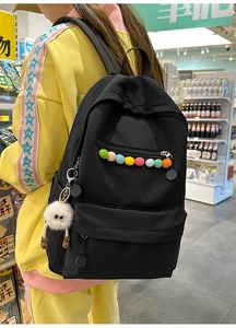 Detail of black nylon backpack with colorful pom-poms and a cute plush monster charm
