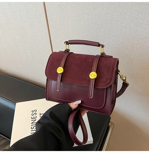 Detail of burgundy crossbody bag featuring suede flap and gold hardware held by hand