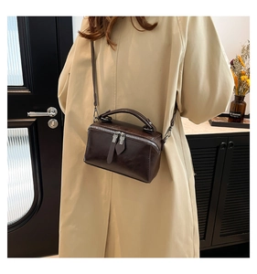 Detail of dark brown mini box bag with top handle and silver double zippers on trench coat