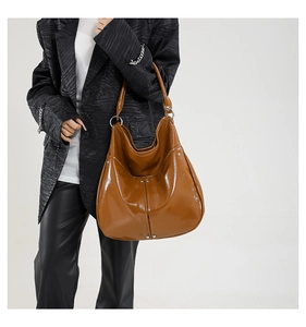 Grand sac hobo marron brillant avec détails de rivets argentés porté par le mannequin