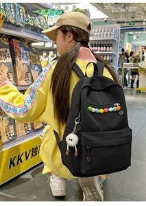 Detail of black canvas backpack with colorful pom-poms and cute monster plush pendant