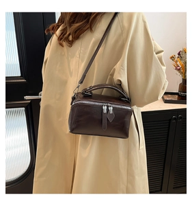 Detail of dark brown leather crossbody box bag with silver zippers on beige coat
