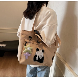 Dettaglio della borsa tote in tela kaki con patch panda e ciondolo a stella sulla spalla