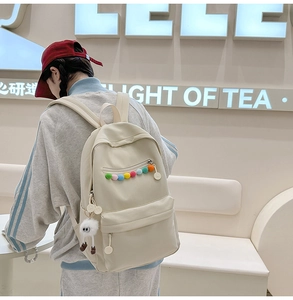 Detail of off-white canvas backpack with colorful zipper charms and plush toy pendant