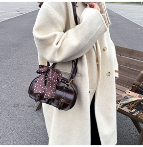 Close-up of a dark brown glossy leather bowling bag with silk scarf on the handle