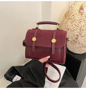 Detail of burgundy leather and suede crossbody bag with gold hardware in artistic setting