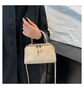 Detail of beige structured box bag with silver zippers and dual carrying options