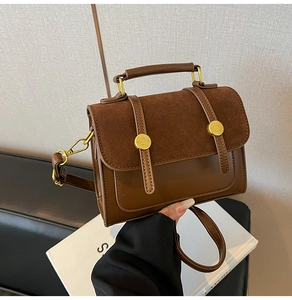 Close-up of a vintage brown crossbody bag with gold buckle and a top handle on a sofa