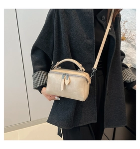 Detail view of cream bucket bag with dual zippers and leather texture on a grey coat