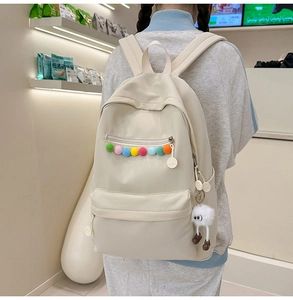 Detail of off-white nylon backpack with colorful plush balls and cute monster charm