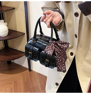 Detail of black vintage Boston bag with gold buckle pockets and polka dot silk scarf