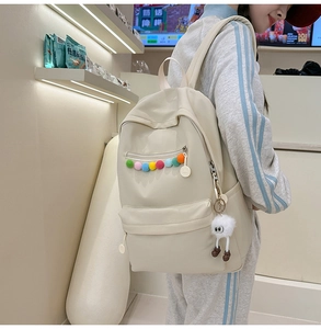 Close-up of cream PU leather backpack with colorful pom-pom and plush monster charm