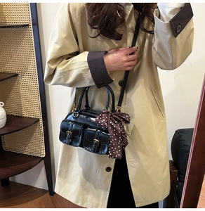 Close-up of black retro Boston bag with metal buckles and decorative polka dot scarf