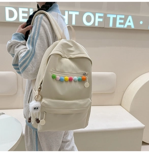 Detail of beige nylon backpack featuring colorful zipper balls and a plush monster charm