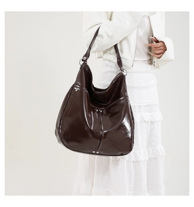 Détail d'un sac hobo marron foncé brillant avec rivets porté sur une veste blanche