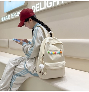 Detail of cream backpack showing colorful pom-poms and cute plush charm in minimalist setting