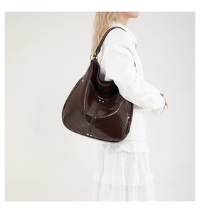 Détail du cabas en cuir verni marron foncé avec des rivets métalliques sur le côté du sac