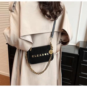 Detail of matte black crossbody bag with gold chain and heart logo on beige coat