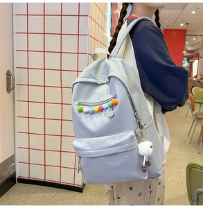 Detail view of a light blue student backpack with a colorful pompom and white plush charm