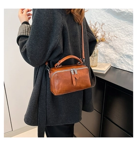 Brown box-style leather handbag shown on model with shoulder strap and dual zipper detail