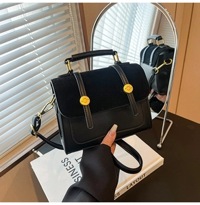 Detail of crossbody bag with black leather stitching and gold circular metal buckles