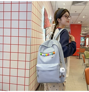 Detail of light blue nylon backpack featuring colorful pom-poms and a white plush charm