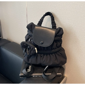 Detail of black pleated nylon backpack featuring a mini side pouch and magnetic flap cover