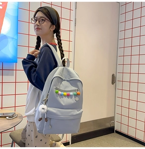 Detail of light blue school backpack with colorful ball zipper and plush pendant charm
