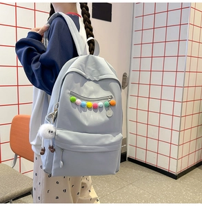 Detail of light blue student backpack with colorful pom-poms and cute plush pendant
