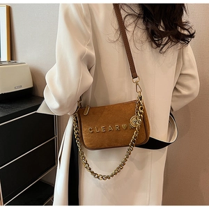 Detail of vintage brown suede crossbody bag with gold chain strap and clear heart charm