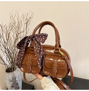 Macro detail of brown leather boston bag with pocket buckles and polka dot silk scarf